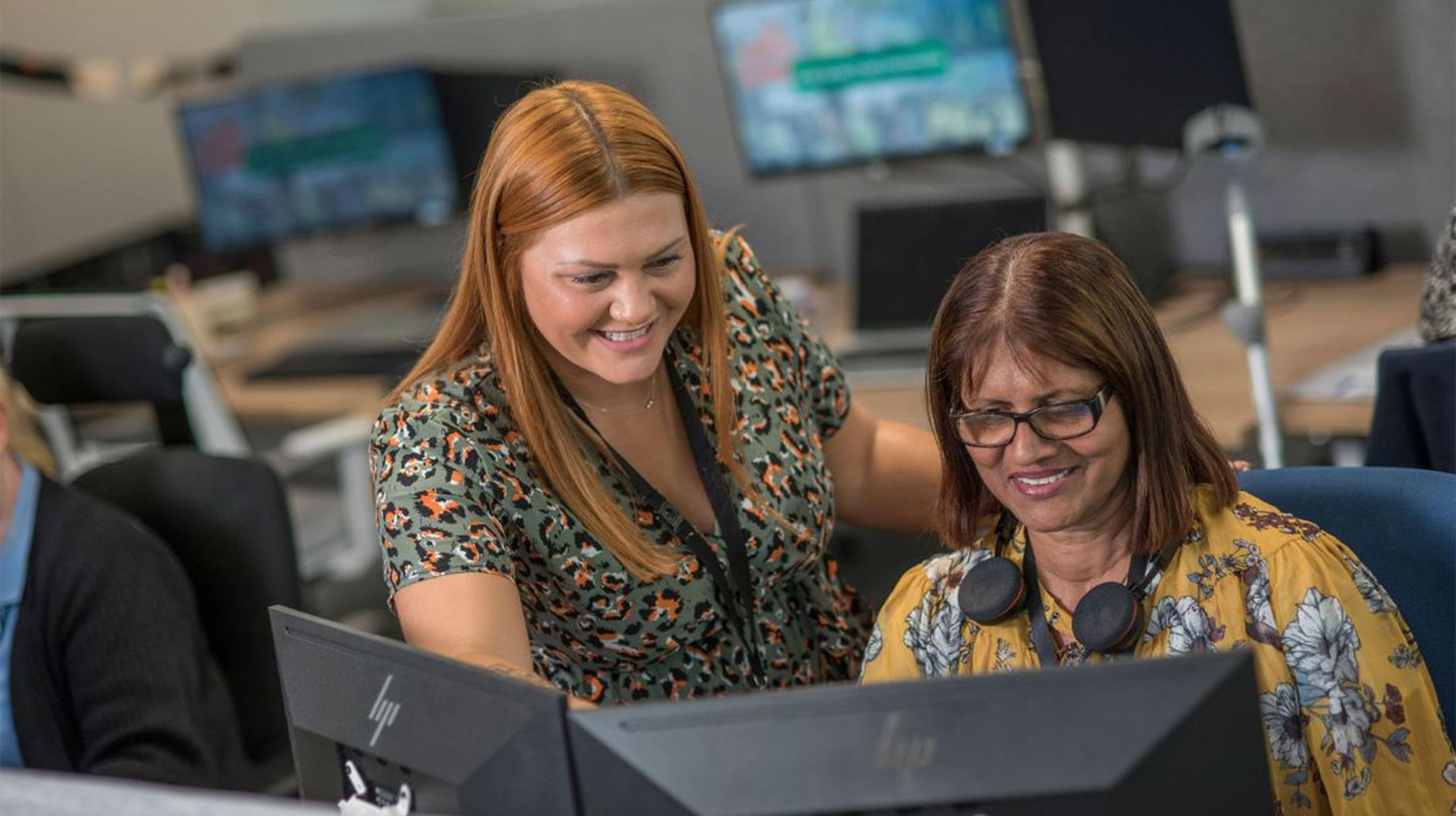 Two women in an Accent office, looking at a computer monitor and smiling