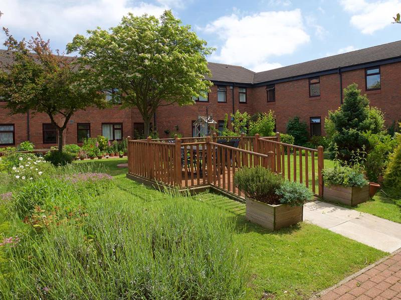 A view of a wooden deck in a garden with a red brick home in the background