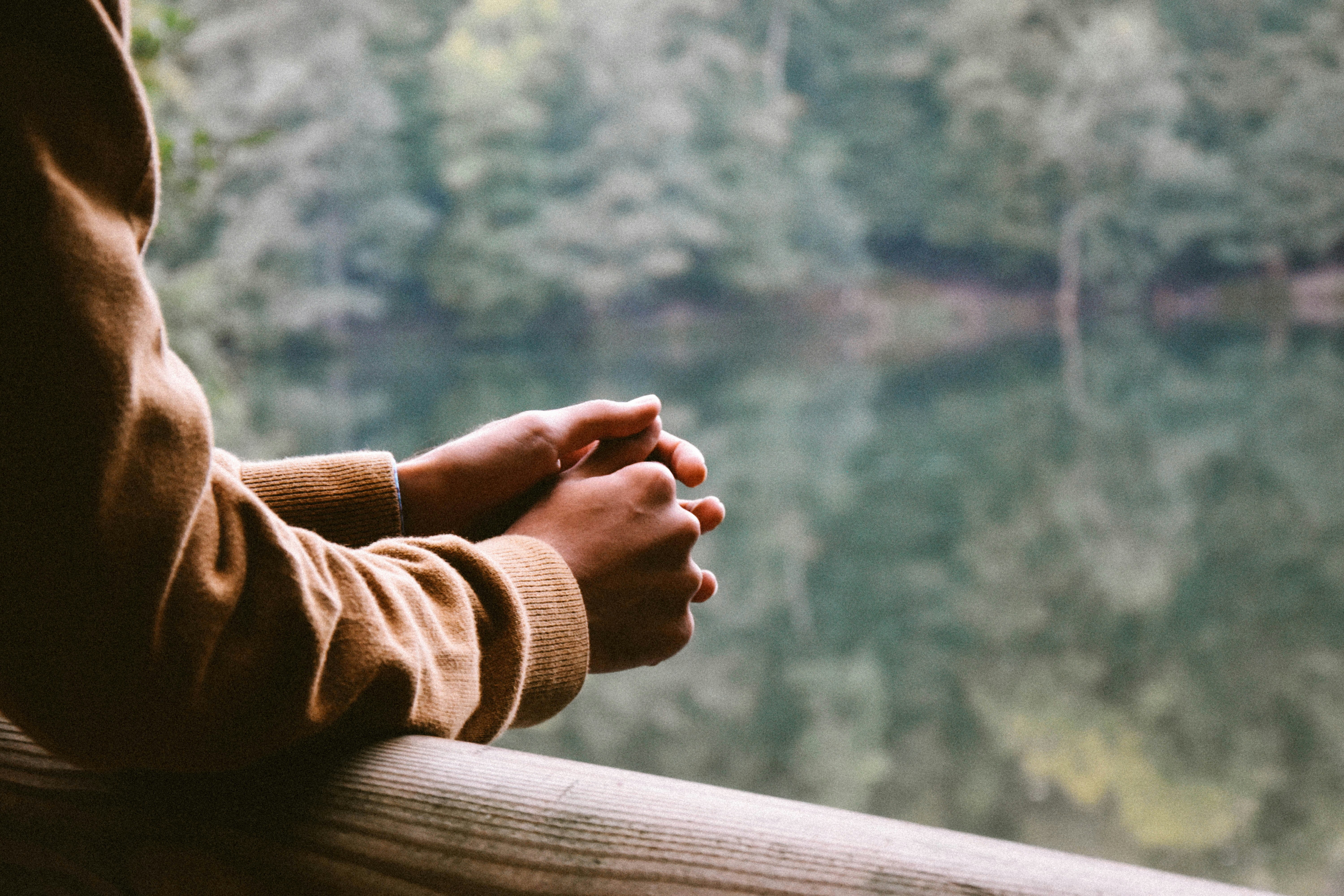 A cropped figure with their hands folded thoughtfully over a fence post