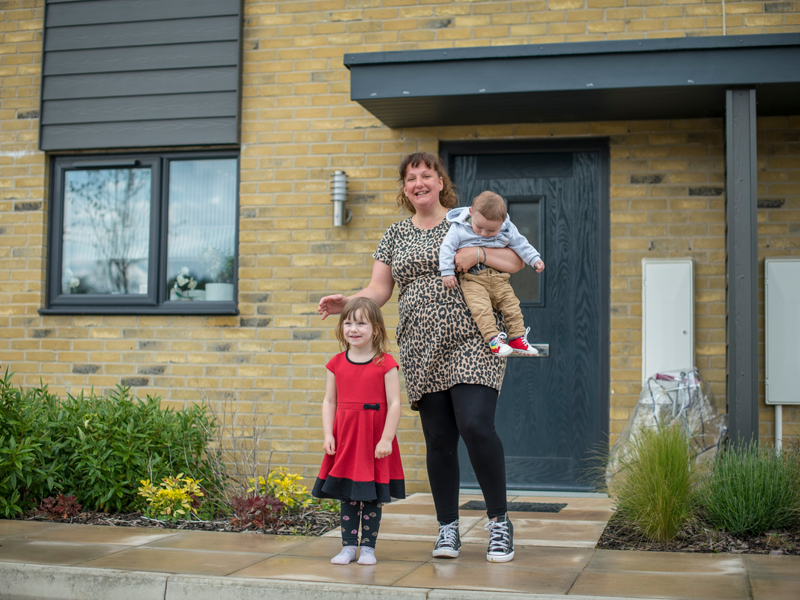 A woman and a child standing outside an Accent home smiling. She's holding a toddler in her arms 