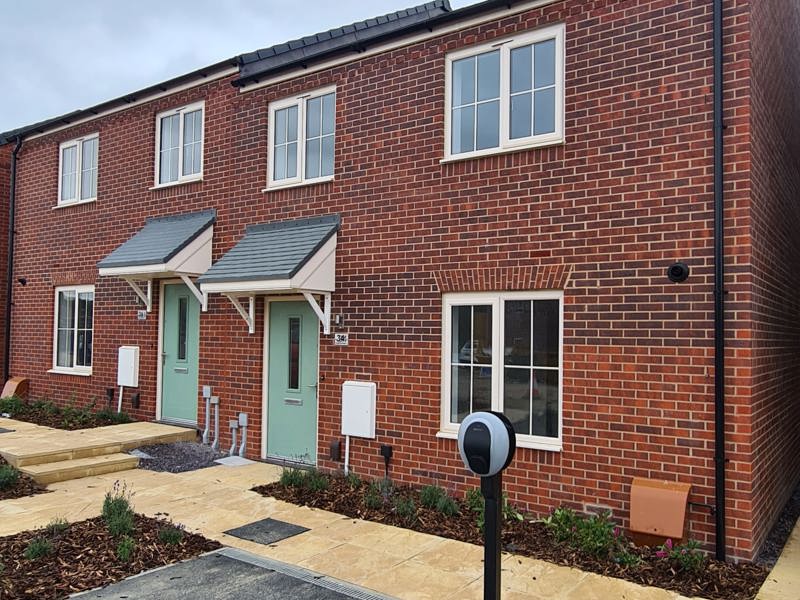 A two-storey red brick housing development with a sage-coloured front door and newly planted flower beds